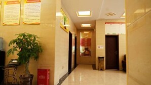 A hotel hallway with a potted plant, a trash bin, and informational posters on the walls. - Xuan'en Junhua Hotel (Xuan'en)