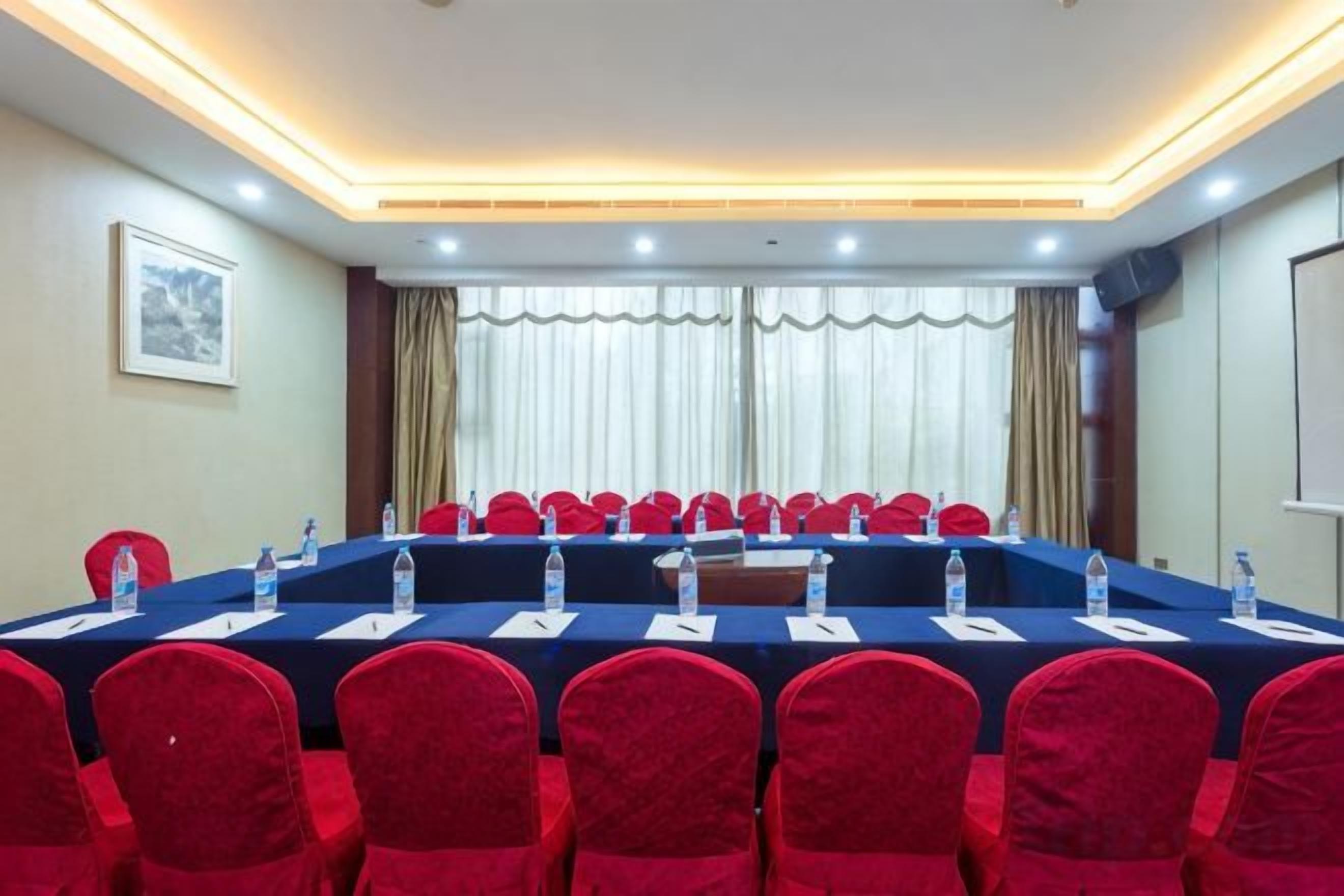 A conference room with a long table, red chairs, water bottles, and a projector screen.