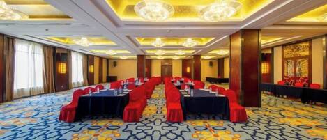 Un salón de conferencias con una larga mesa dispuesta para reuniones, alfombra estampada y candelabros.