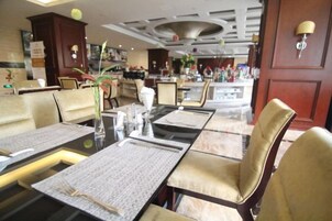 A hotel dining area with tables set for multiple guests, chairs, and a bar area in the background.