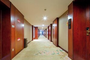 A hotel corridor with wooden doors, a trash bin, and a carpeted floor. - Merlinhod Hotel (Yuncheng Airport, North Railway Station) (Yuncheng)
