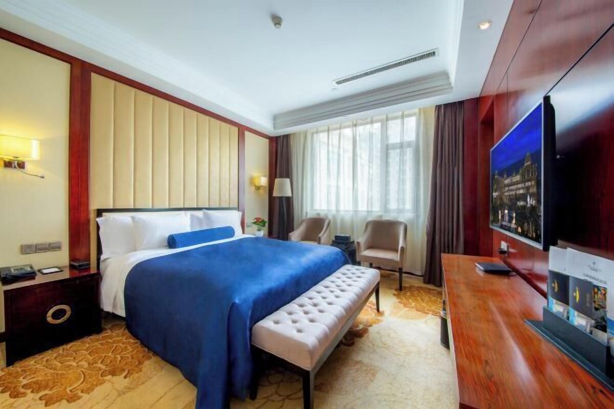 A hotel room with a large bed, a television, a desk, and a seating area.