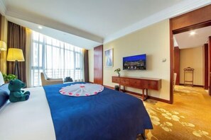 A hotel room with a large bed, a TV on the wall, a desk with a lamp, and a view of the outdoors through large windows. - Merlinhod Hotel (Yuncheng Airport, North Railway Station) (Yuncheng)