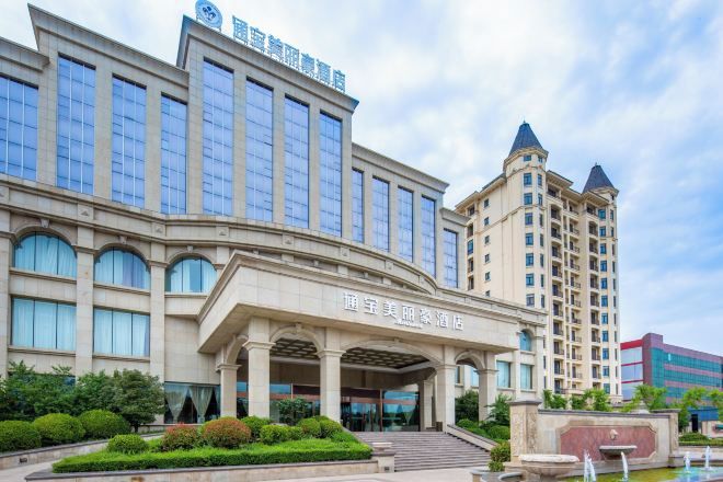 Un hotel con una entrada destacada, varios pisos y una fuente al frente.
