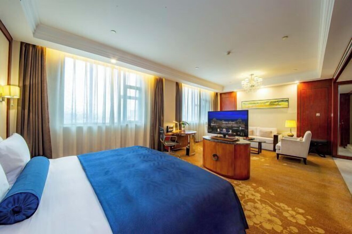 A hotel room with a large bed, a television, a desk, and a seating area.