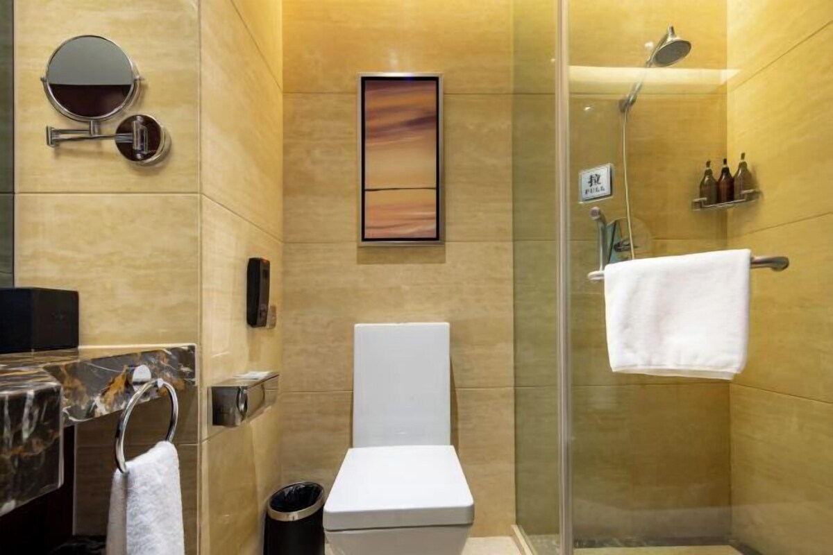 A modern bathroom with a toilet, a glass-enclosed shower, a marble sink, and a towel rack.