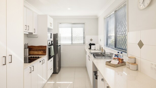 A modern kitchen with white cabinetry, a stainless steel refrigerator, a wooden cutting board, and a window with blinds. - Family Rocklea 3BR | Spacious | Parking | 219D3 (Rocklea)