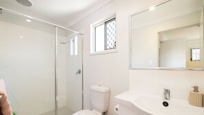 Un baño con cabina de ducha de vidrio, inodoro, lavabo y ventana con celosía decorativa.
