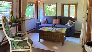A cozy room with a wooden ceiling, a blue sofa, a floral armchair, and a coffee table. - FARE TEAK with PALAPA and shared pool (Moorea-Maiao)