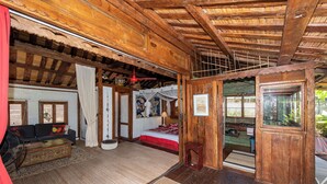 A wooden cabin with a living area, a bed, and a small dining area. - FARE TEAK with PALAPA and shared pool (Moorea-Maiao)