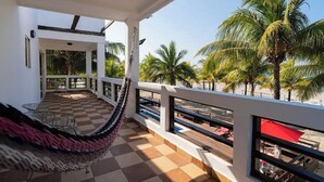 Een balkon met een geruite vloer, een hangmat en uitzicht op palmbomen en een strand.