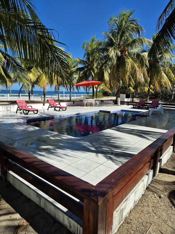 A pool area with lounge chairs, a red umbrella, and palm trees.
