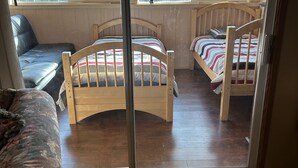 A room with two wooden beds, a ceiling fan, and large windows offering a view of trees. - Charming 4-bedroom mobile home with WiFi and AC in Timberon (Timberon)