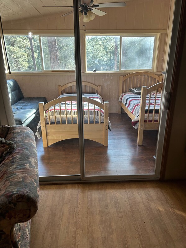 A room with two wooden beds, a ceiling fan, and large windows offering a view of trees.