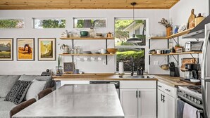 Een moderne keuken met witte kasten, een houten aanrecht en een inbouwfornuis. Daarboven bevinden zich planken met diverse keukenbenodigdheden.