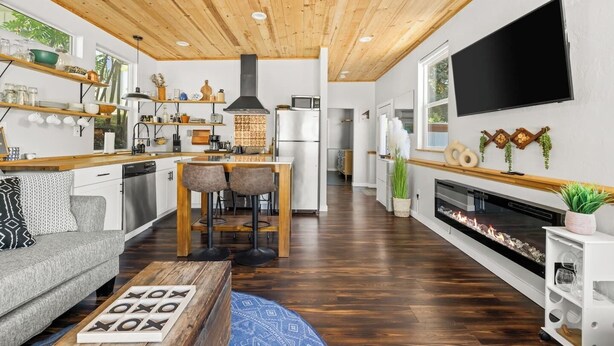 Een moderne keuken met houten plafond, een eethoek met twee stoelen, een open haard en een aan de muur bevestigde televisie.