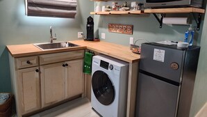 Una cocina compacta con lavadora, refrigerador, microondas y estantes de madera arriba.