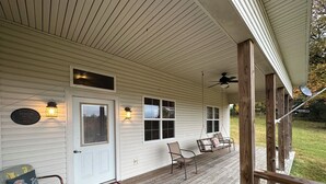 A covered porch with a white door, two windows, a hanging chair, and a ceiling fan.