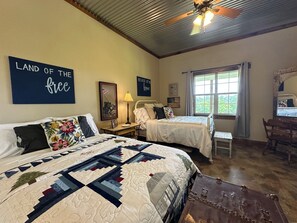 Een slaapkamer met twee bedden, een houten vloer, een plafondventilator en een raam met gordijnen.