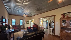 A spacious living room with a high ceiling, a fireplace, and a view into the kitchen.