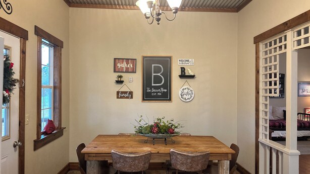 A dining area with a wooden table, two chairs, a chandelier, and wall decorations including a 'B' sign and 'family' sign.