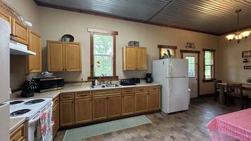 A kitchen with wooden cabinets, a white refrigerator, a stove, a sink, and a window with a flower.