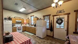A kitchen with wooden cabinets, a white refrigerator, a stove, and a table with a red and white checkered tablecloth.