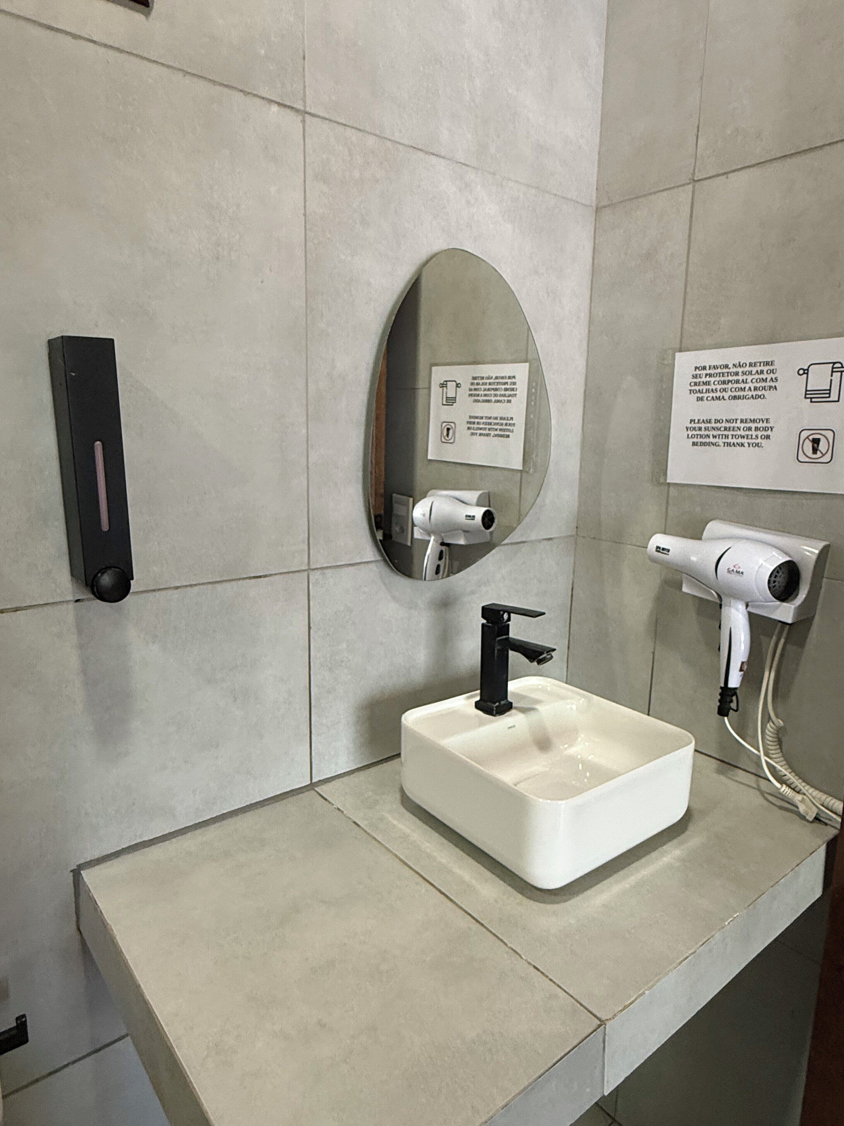 Casa de banho com lavatório branco, torneira preta, secador de mãos e espelho.