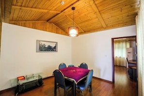 Zona pranzo con soffitto in legno, tavolo con sedie, tavolino in vetro e lampadario.