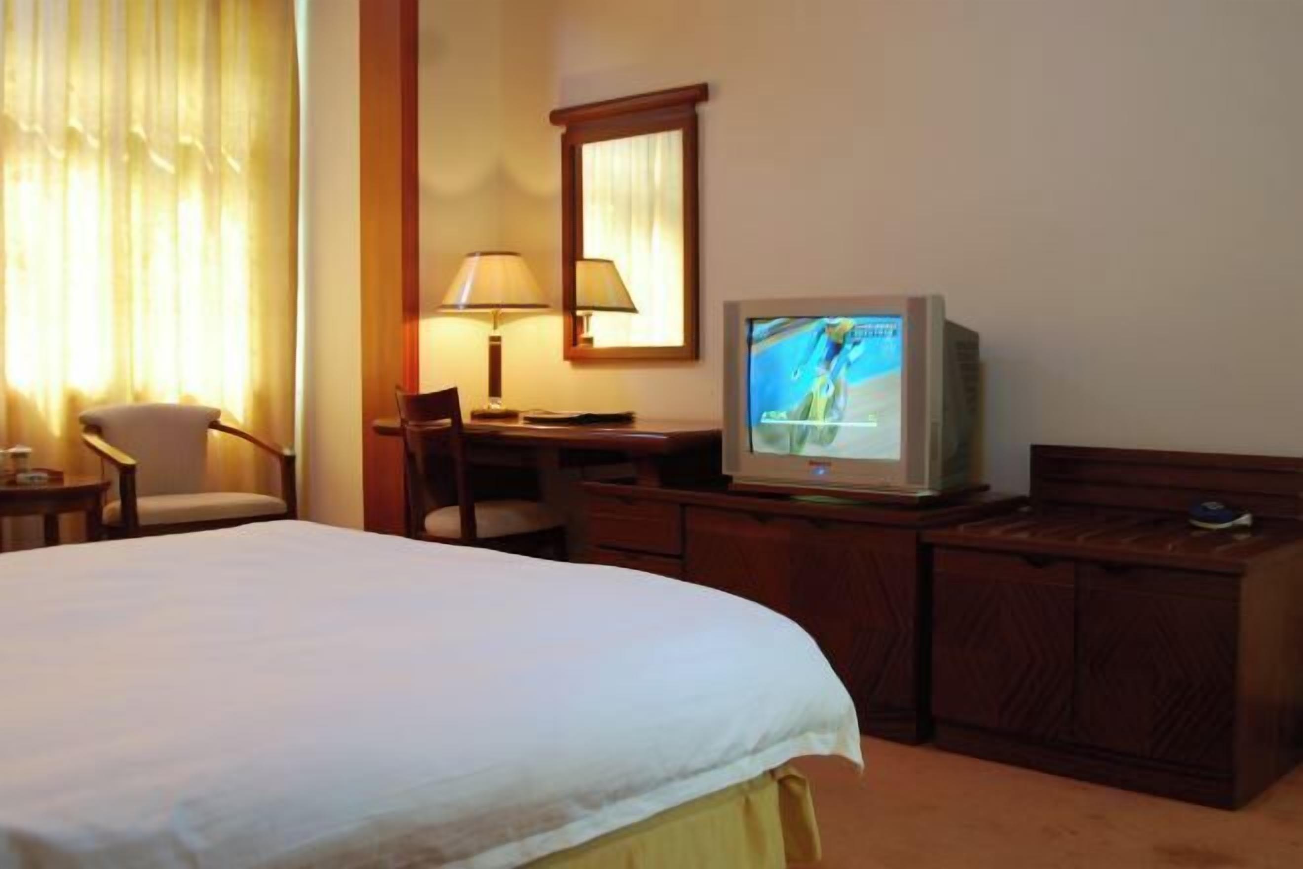 A hotel room with a bed, a desk with a computer, a chair, a television, and a window with curtains.