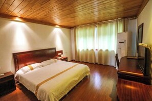 Ein Hotelzimmer mit Holzboden, einem Bett mit weißer Bettwäsche, einem Nachttisch, einem Schreibtisch mit Stuhl und einem Fenster mit Vorhängen.