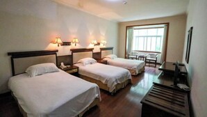 A hotel room with three beds, bedside lamps, a desk with a chair, a window, and a desk lamp. - Jin Xiu Hotel (Yushan)