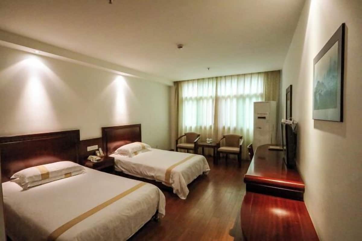 A hotel room with two beds, a desk, a chair, and a television.