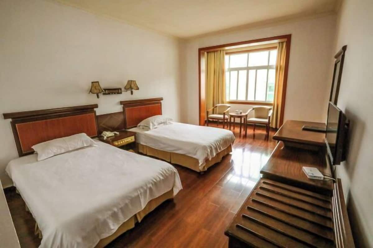A hotel room with two beds, a desk, a chair, a TV, and a window with curtains.