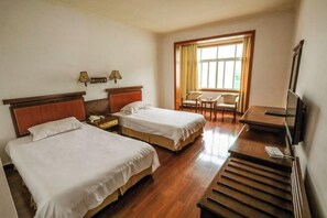 Ein Hotelzimmer mit zwei Betten, einem Schreibtisch, einem Stuhl, einem Fernseher und einem Fenster mit Vorhängen.