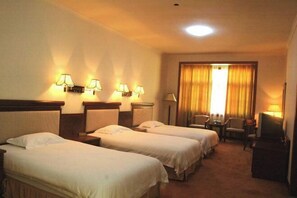 Ein Hotelzimmer mit zwei Einzelbetten, einem Schreibtisch, einem Stuhl und einem Fernseher.