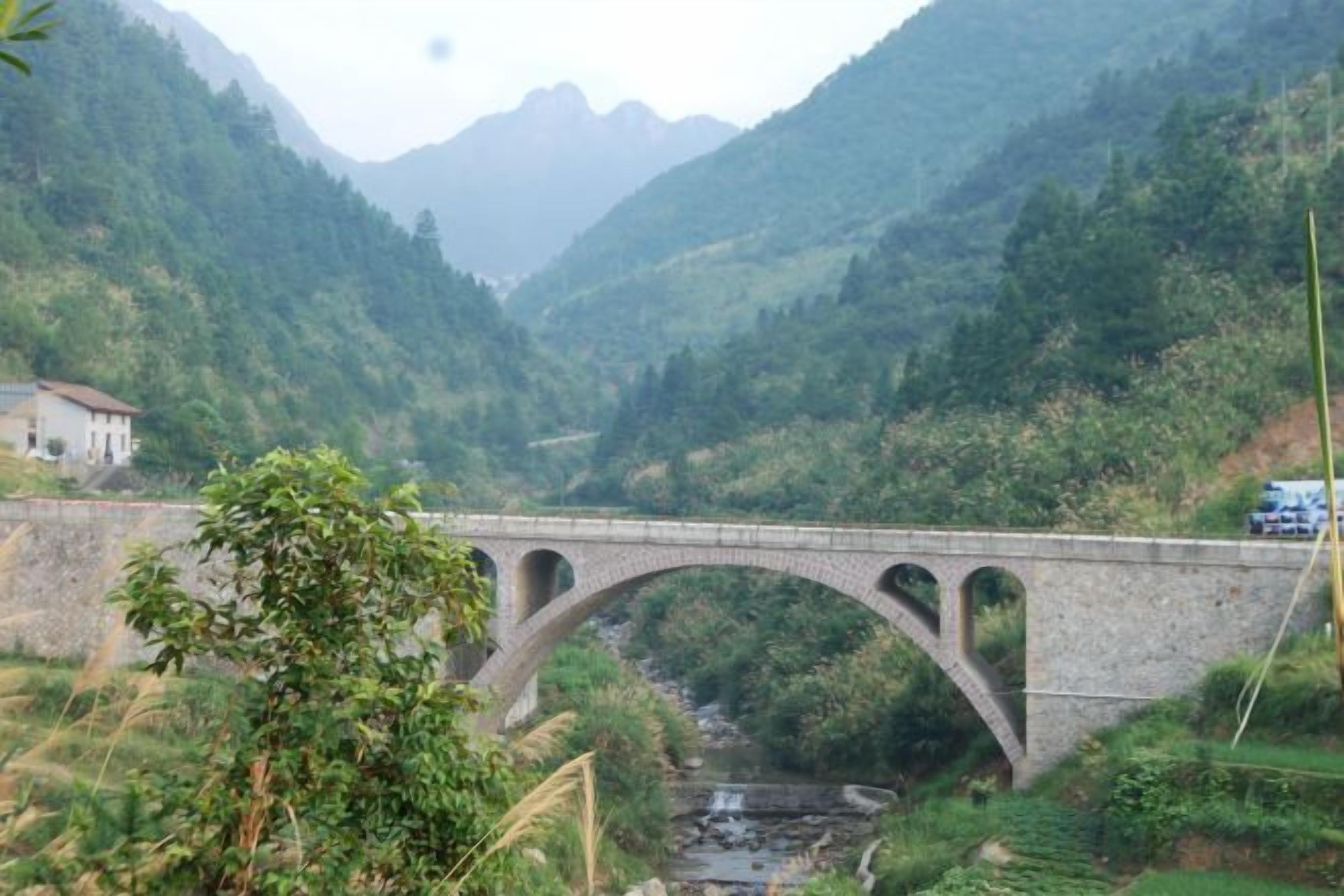 A stone bridge over a river with a mountainous backdrop.