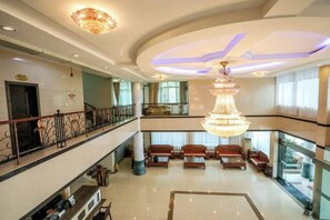 A hotel lobby with a grand chandelier, seating area, and a balcony with a railing.
