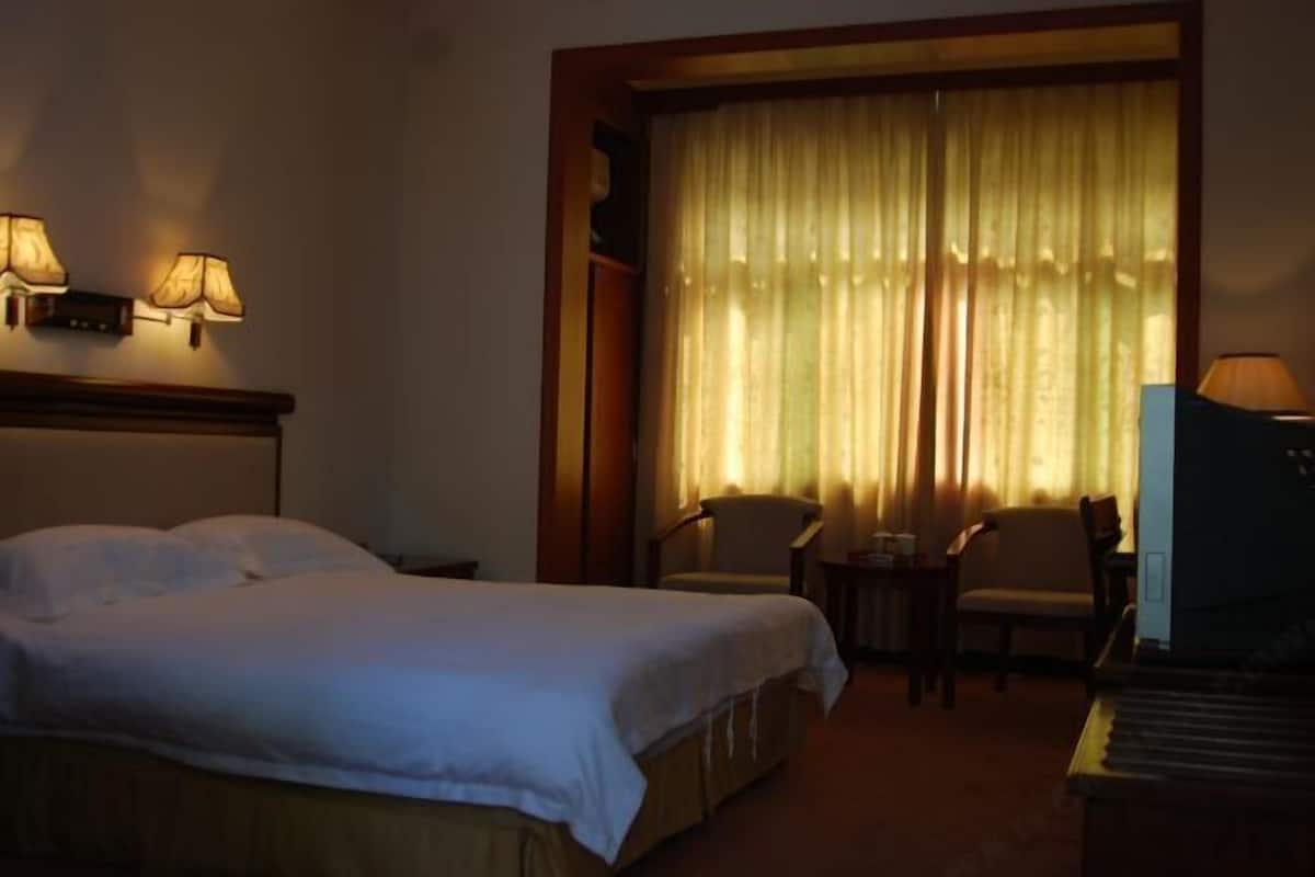 A hotel room with a bed, two chairs, a small table, and a television.