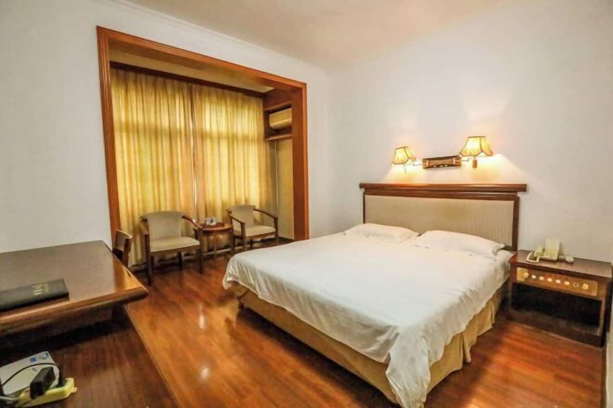 A hotel room with a bed, a desk, a chair, a lamp, and a nightstand.