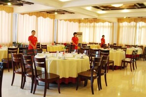 Restaurante com mesas redondas, cadeiras e funcionários com uniformes vermelhos.