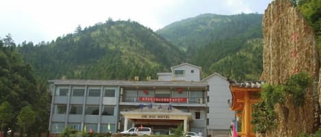 A hotel with a modern facade, a parking area, and a mountainous backdrop.