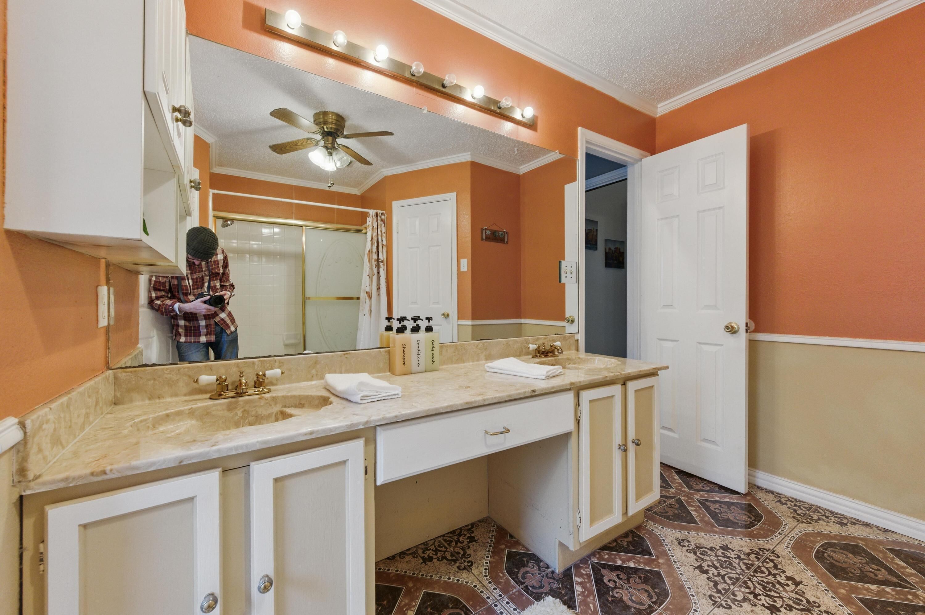 Une salle de bain avec un meuble-lavabo, un ventilateur de plafond et un miroir avec éclairage intégré.