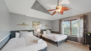 A hotel room with two beds, a ceiling fan, a window with curtains, and wall art.