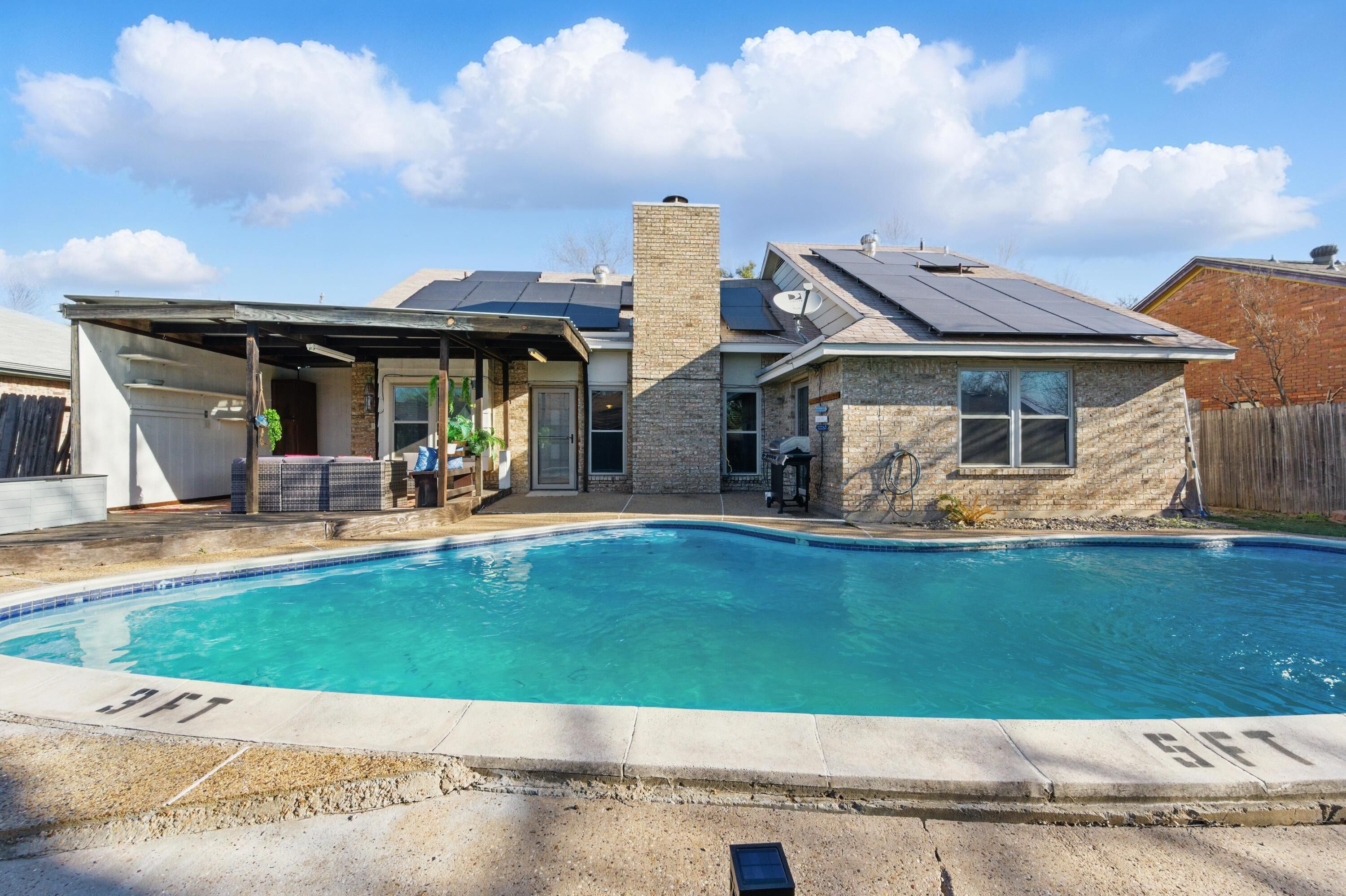 Um imóvel residencial com piscina, varanda coberta e uma casa de tijolos com painéis solares.