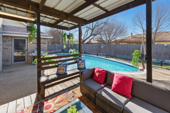 A covered patio with a pool, outdoor seating, and hanging plants.