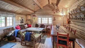 L’intérieur d’un chalet confortable en bois, avec un coin repas, un ensemble de canapés et une cheminée.
