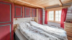 Une chambre de style cabane avec un plafond en bois, un lit simple, une fenêtre avec des rideaux et une petite commode.