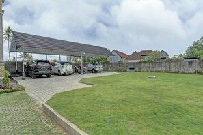 Un espace de stationnement couvert abritant plusieurs voitures, une pelouse verdoyante et un mur en pierre.