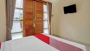 Ein Hotelzimmer mit Bett, Vorhängen, einem Fernseher und einer Schiebetür.